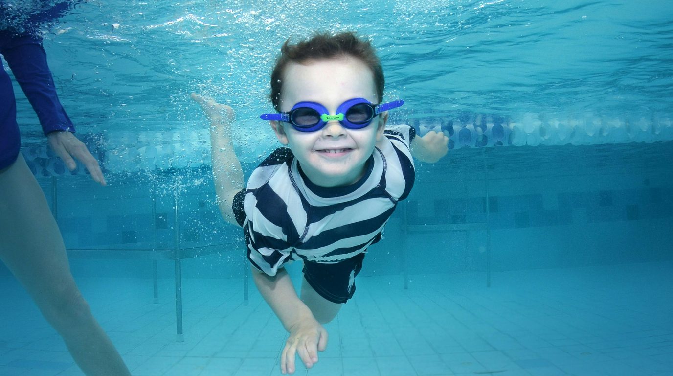Child swimming underwater wearing goggles, smiling