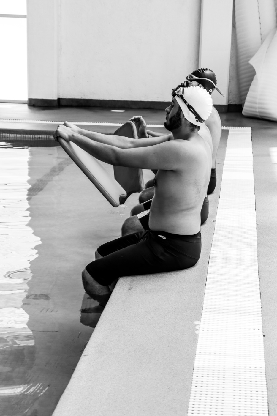 Two swimmers seated poolside preparing with kickboards before a session